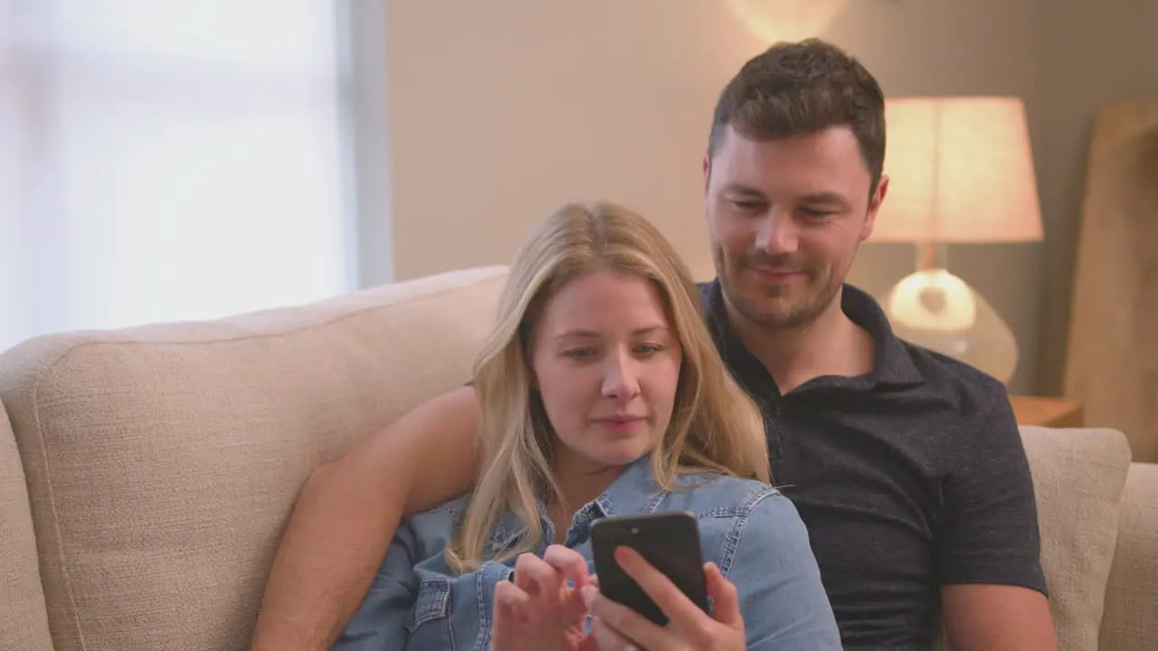 Evening shot of couple relaxing on sofa at home looking at mobile phone shot in slow motion