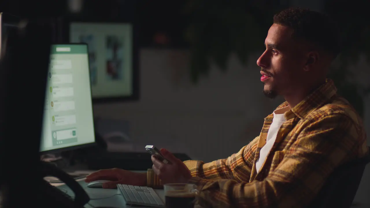 Businessman Working Late In Office With Face Illuminated By Computer Screen Using Mobile Phone