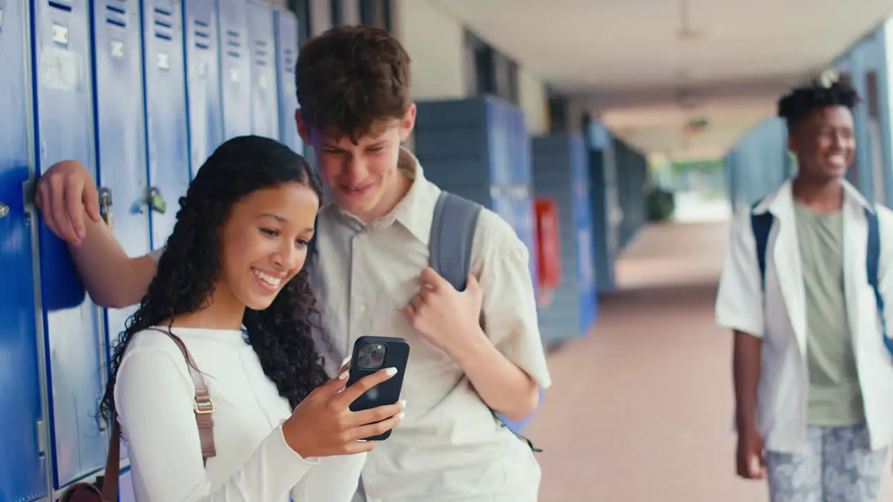 Two High School Or Secondary Students Looking At Social Media Or Internet On Phone By Lockers