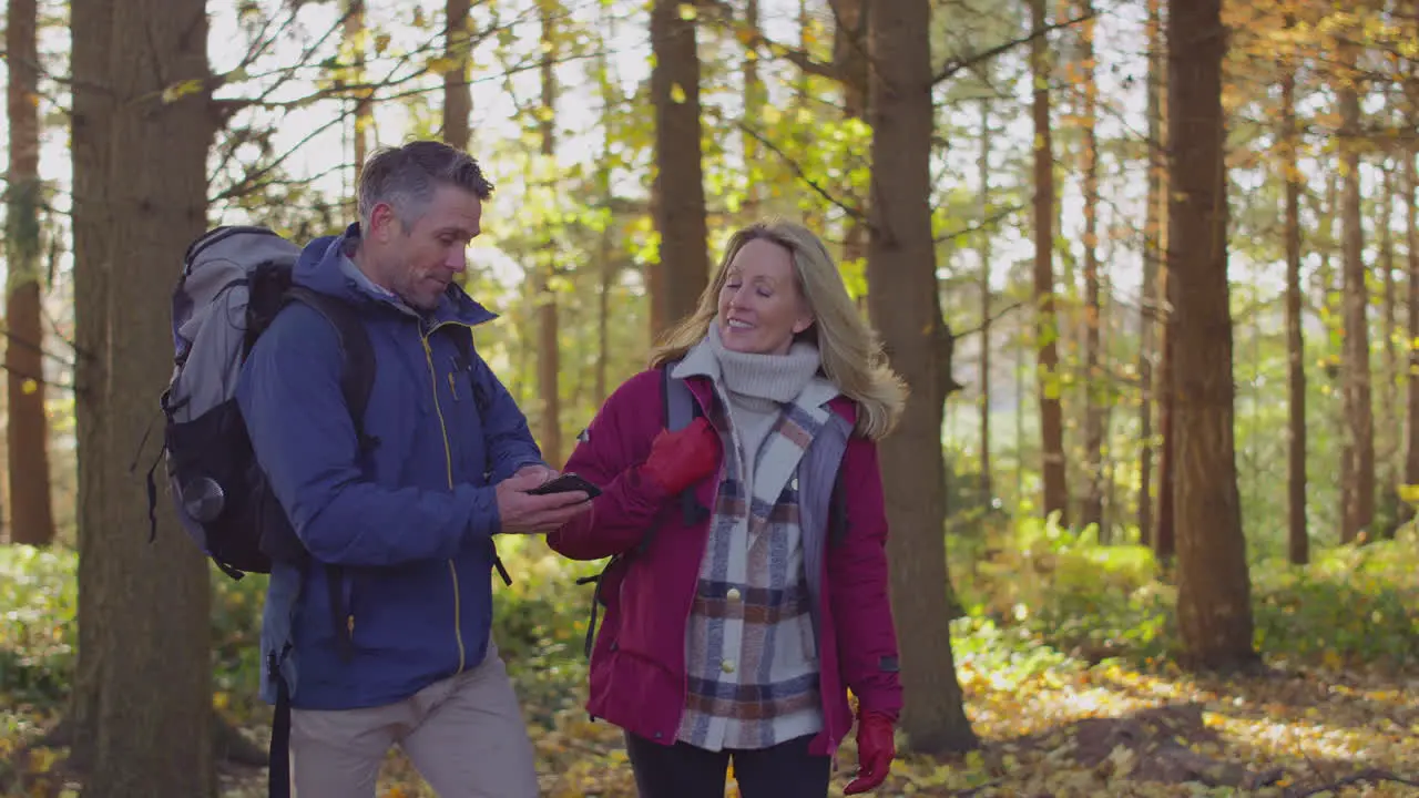 Mature couple walking through fall or winter countryside looking at navigation app on mobile phone to find way shot in slow motion