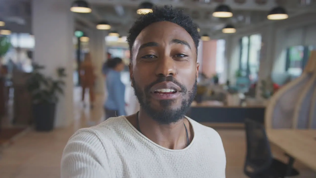 Portrait Of Young Businessman Vlogging Into Camera In Modern Open Plan Office