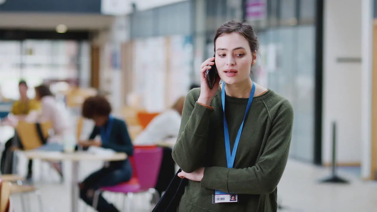 Smiling Female College Student Talking On Mobile Phone In Busy Communal Campus Building