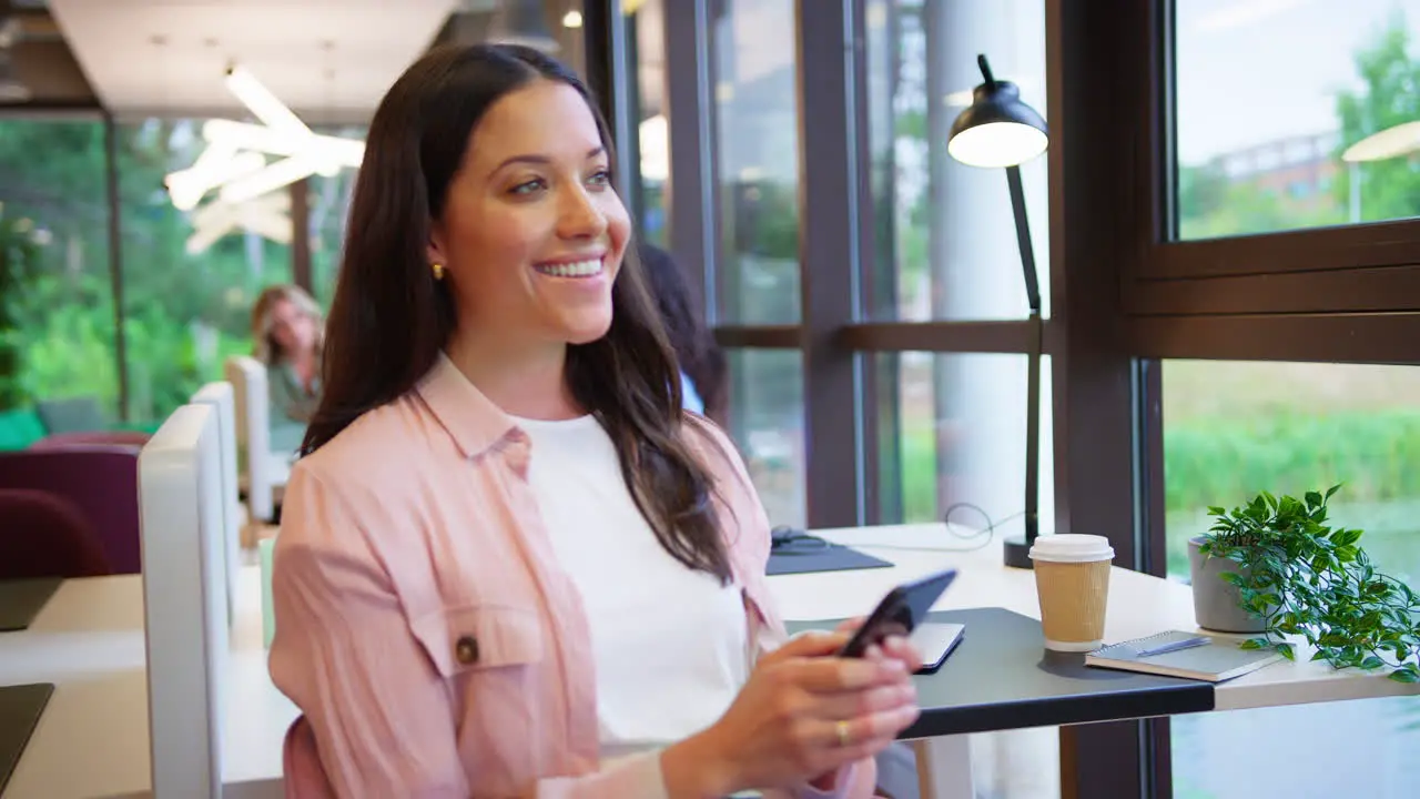 Businesswoman Sitting Taking A Break At Desk In Office Texting Or Browsing On Mobile Phone