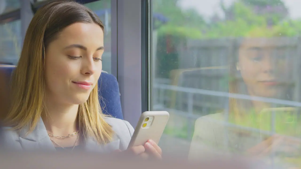 Close Up Of Businesswoman Commuting To Work On Train Looking At Mobile Phone