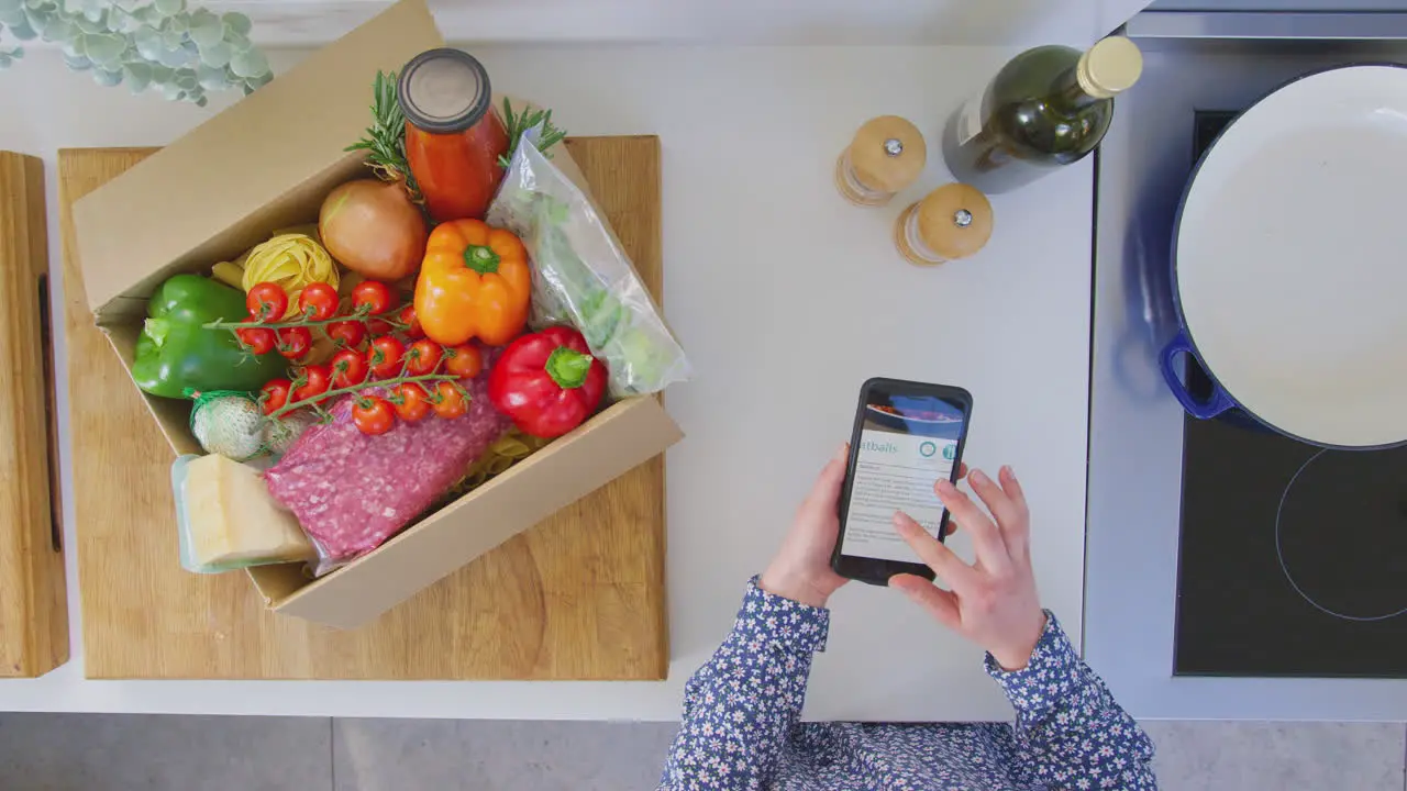 Overhead shot of woman in kitchen with fresh ingredients looking at online recipe on mobile phone shot in slow motion