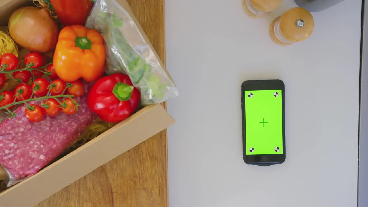 Overhead shot of box of fresh ingredients next to green screen mobile phone shot in slow motion