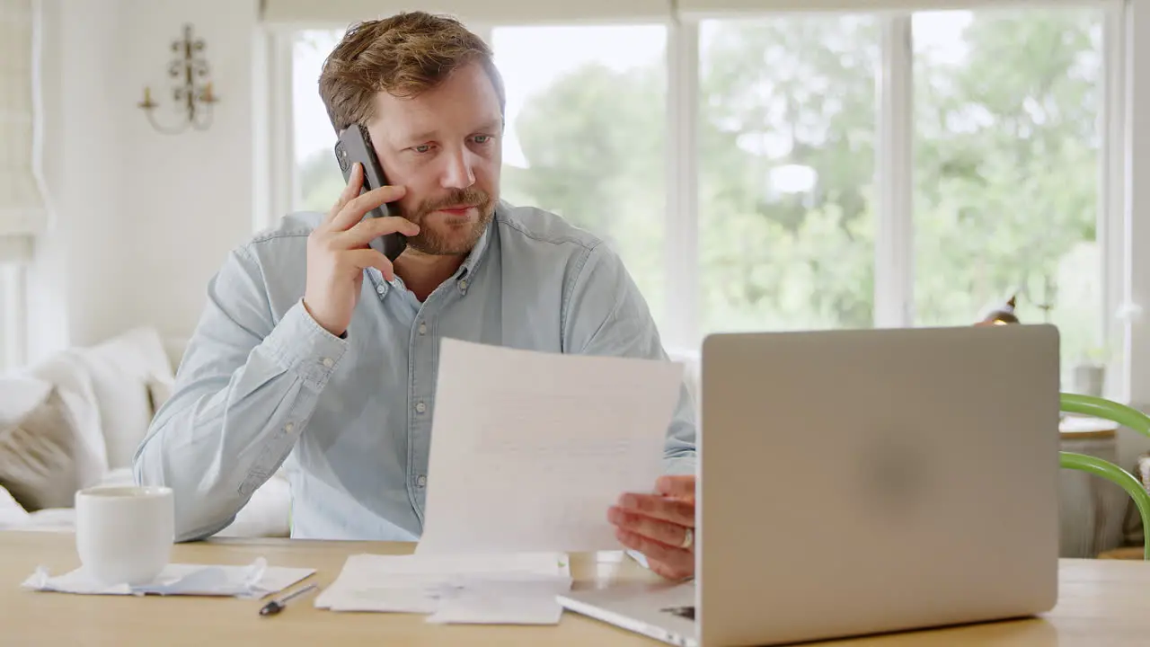 Man On Phone Call At Home With Laptop Computer Reviewing Domestic Finances