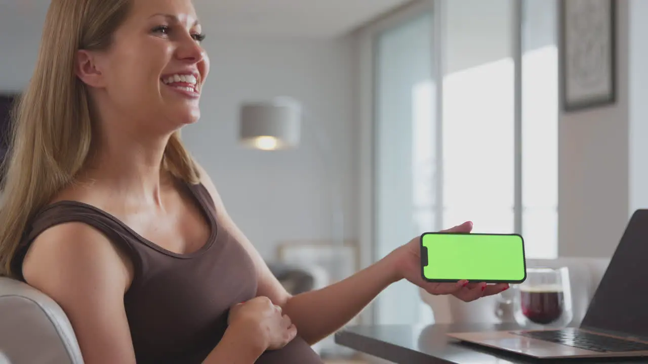 Smiling Pregnant Woman At Home Working On Laptop Holding Green Screen Mobile Phone