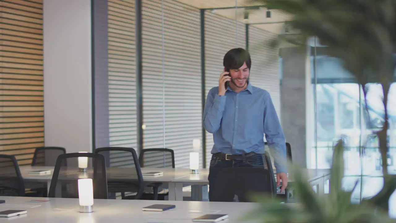 Businessman On Phone Call Walking Through Modern Open Plan Office