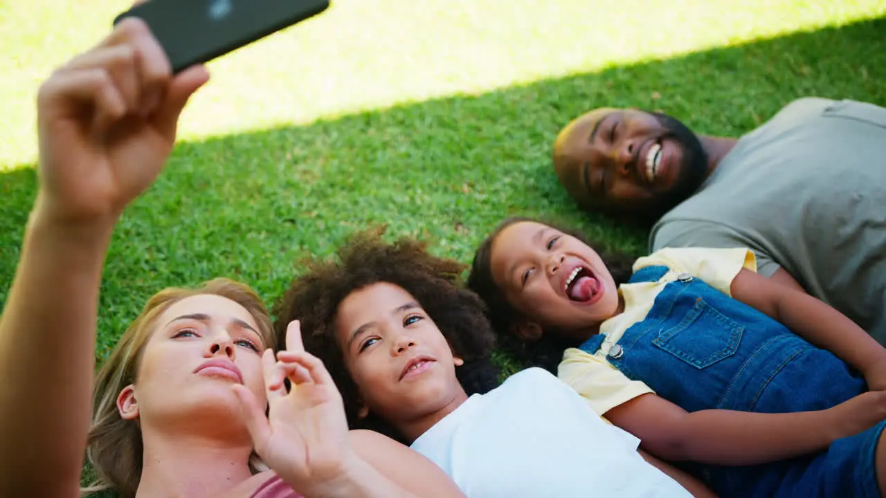 Overhead Shot Of Multi-Racial Family Lying On Grass Taking Selfie On Mobile Phone