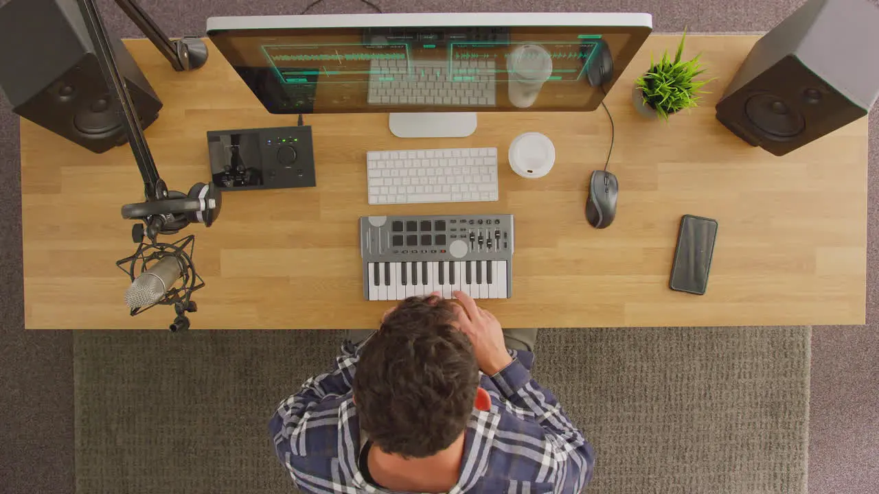 Overhead View Of Male Musician At Workstation With Keyboard And Microphone In Studio