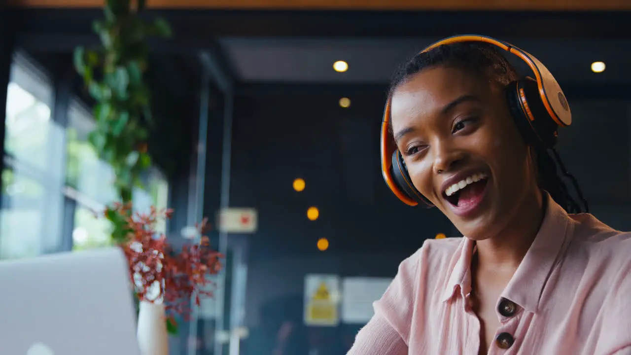 Young Businesswoman Wearing Wireless Headphones Making Video Call On Mobile Phone In Coffee Shop