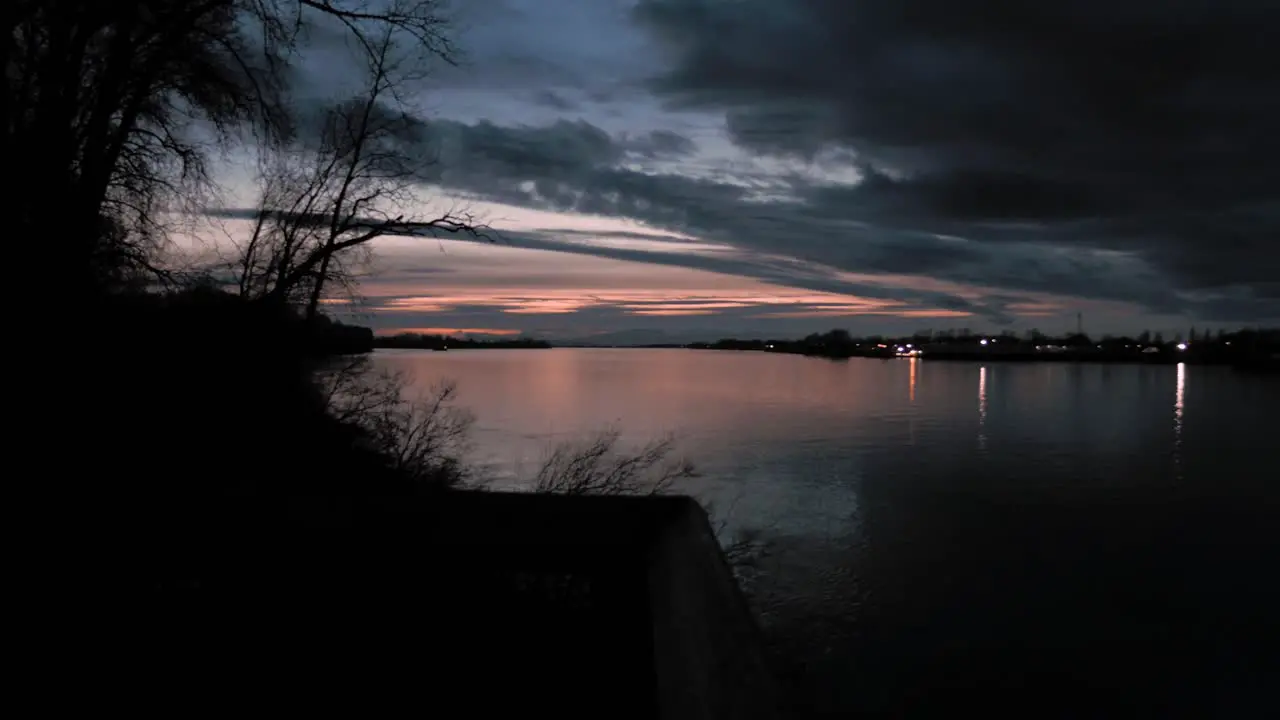 Pan left view of dark clouds over still river waters with dramatic clouds and colours in the sunset sky