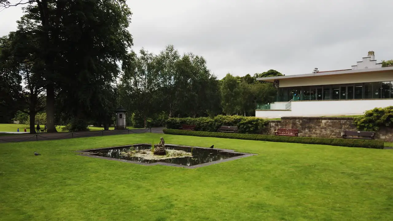 Dunfermline glen Fife Scotland with lawn pond and fountain with a crow stopping to drink and the glen pavilion in the background