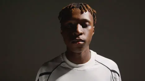 Studio Portrait Of Young Male Footballer Or Sportsperson Putting On Club Kit Shirt