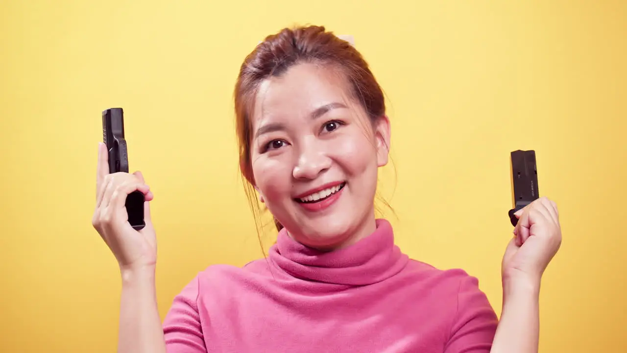 Close up Smiling Asian woman checking handgun to safety for ammo on bright yellow background-1