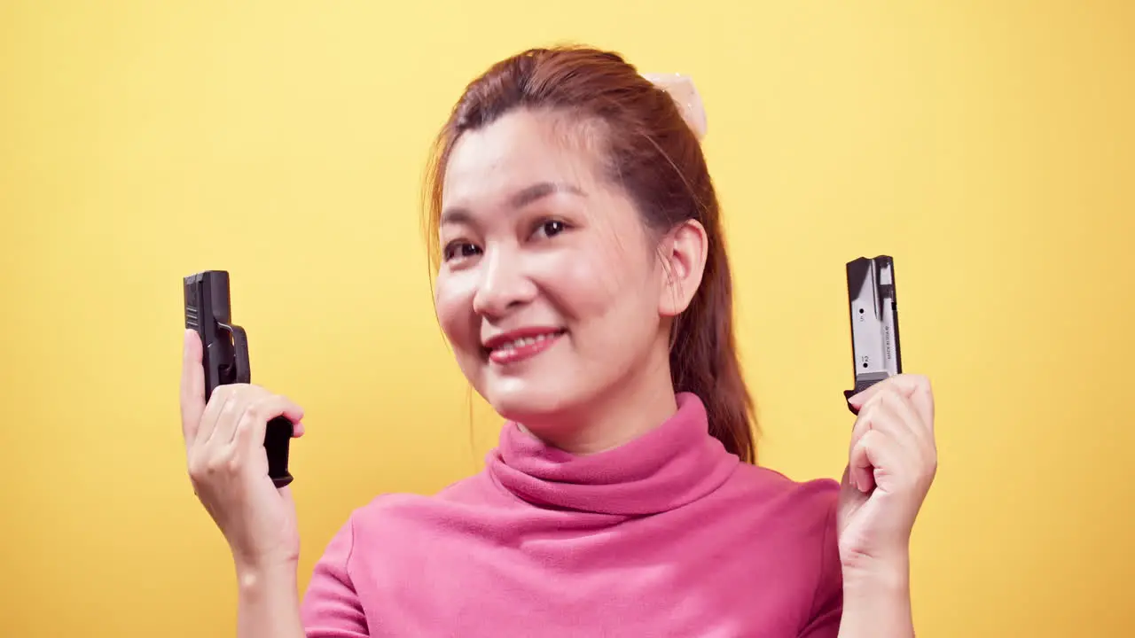 Close up Smiling Asian woman checking handgun to safety for ammo on bright yellow background