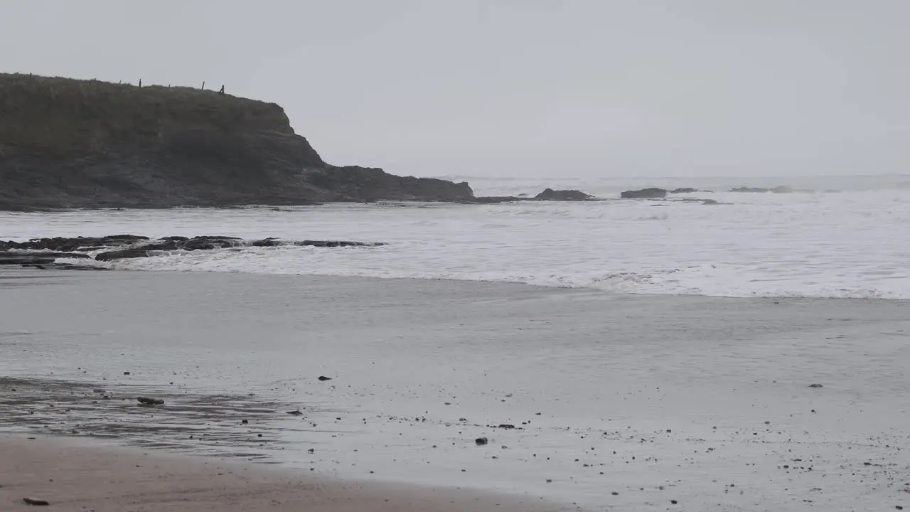 Cliffs near beach are fogged up and hit by waves during stormy winter day