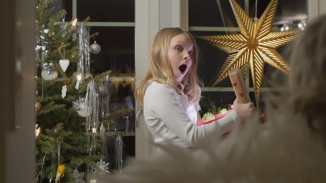 Young girl at Christmas tree opens glowing present