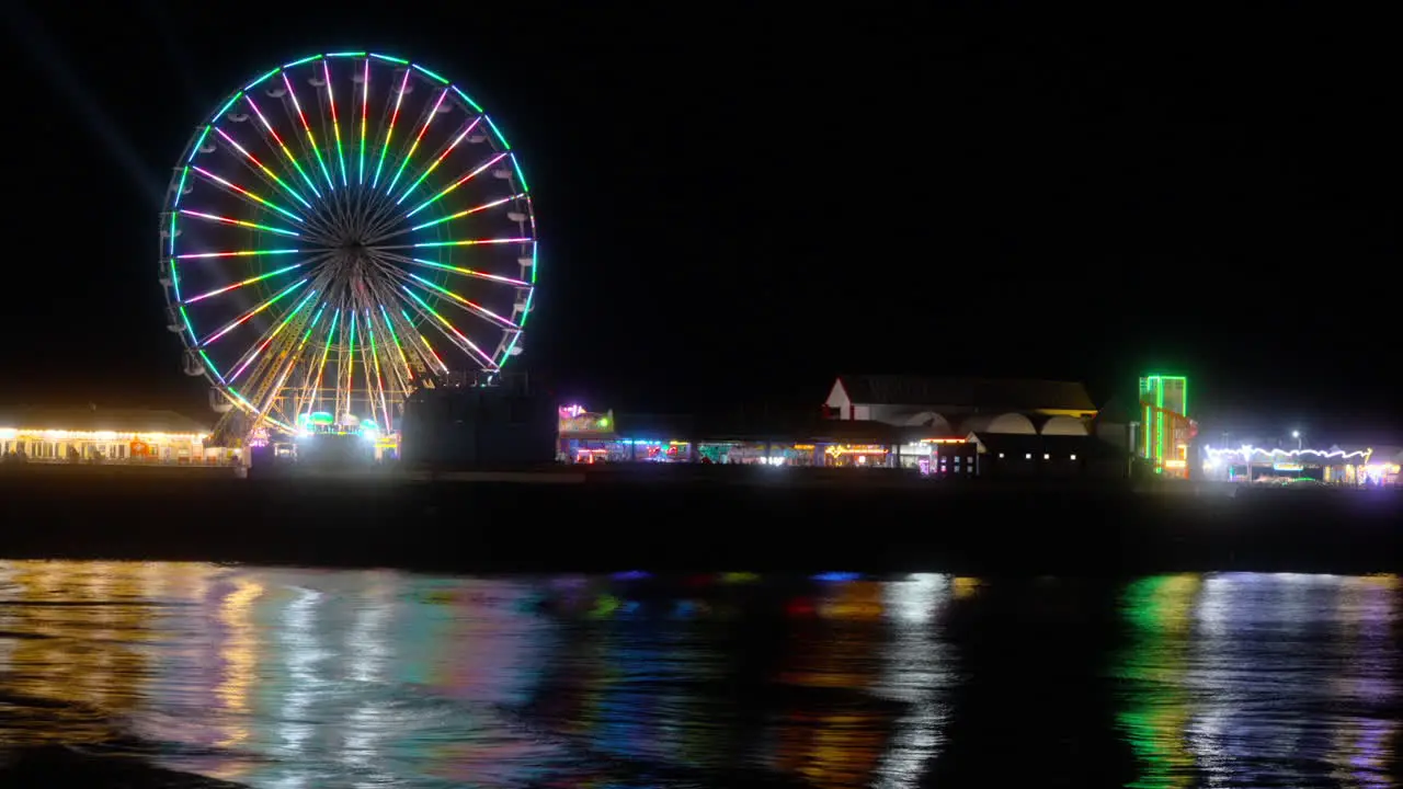 Big wheel ride and amusements at night with lights reflecting off the incoming tide at Central Pier Blackpool Lancashire England UK