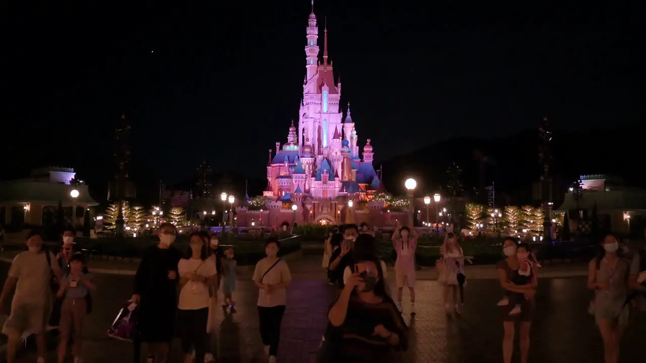 Visitors take photos and walk through the park before the American amusement park Disneyland Resort closes as the iconic Disney's Castle is seen in the background in Hong Kong