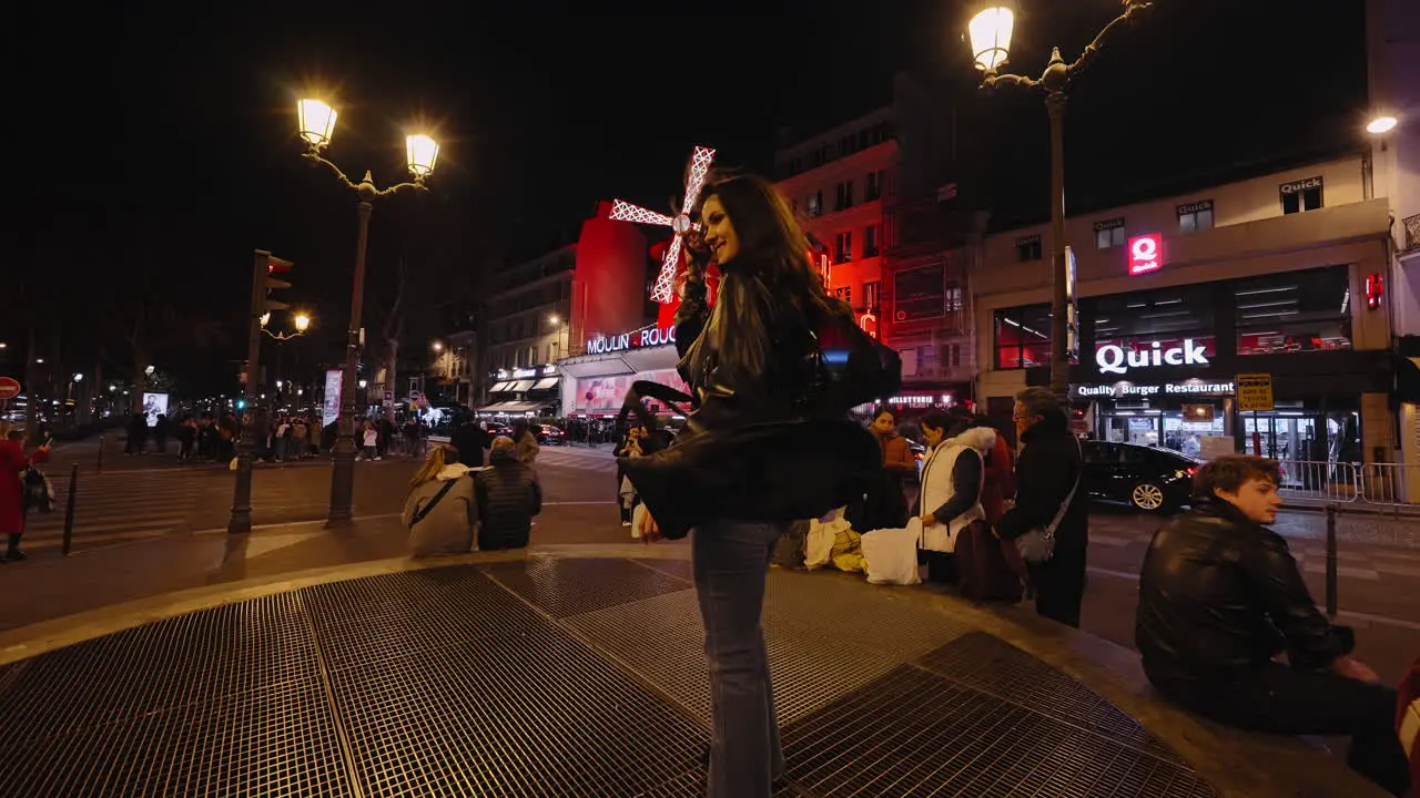 Tourists gather on sidewalk in front of Moulin Rouge in Paris France night time