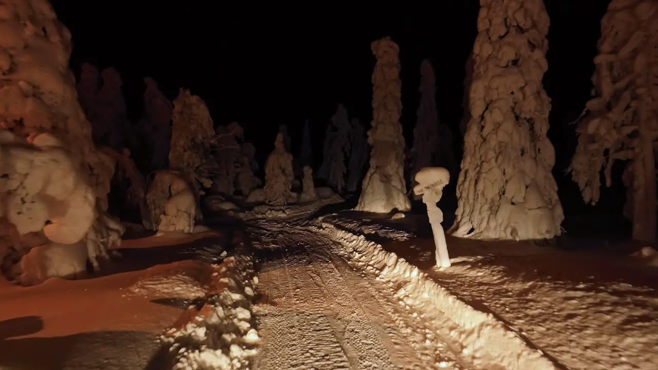 Aerial view flying along a trail in middle of snow covered trees night in Lapland