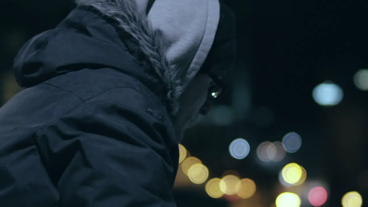 Hooded man with glasses looks out over the city on a cold night