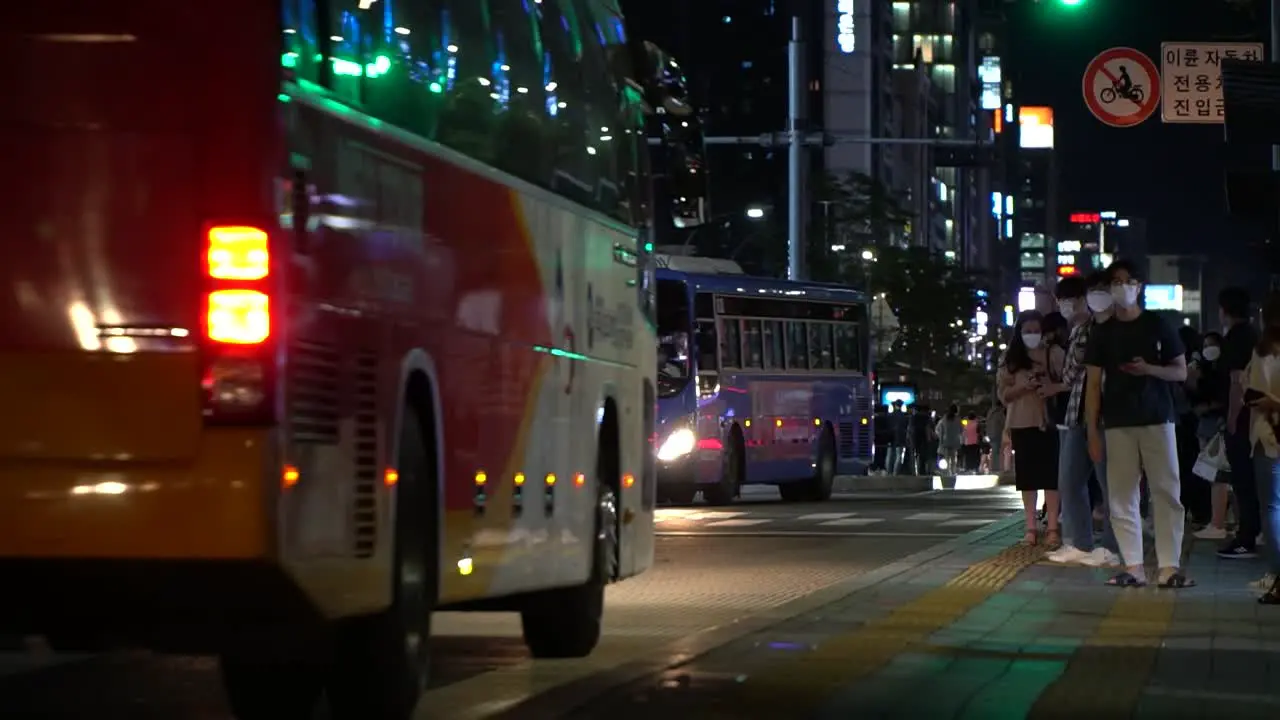 Nighttime view of the Gangnam bus stop station in downtown Seoul with people lined up to ride wearing face masks to protect against COVID infection