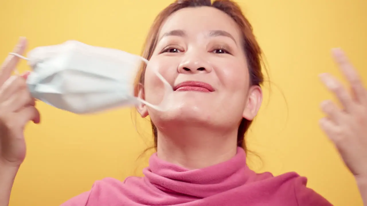 Close up Asian woman smiling and taking off the protective mask for fresh air after the CIVID-19 situation unravels with the yellow background