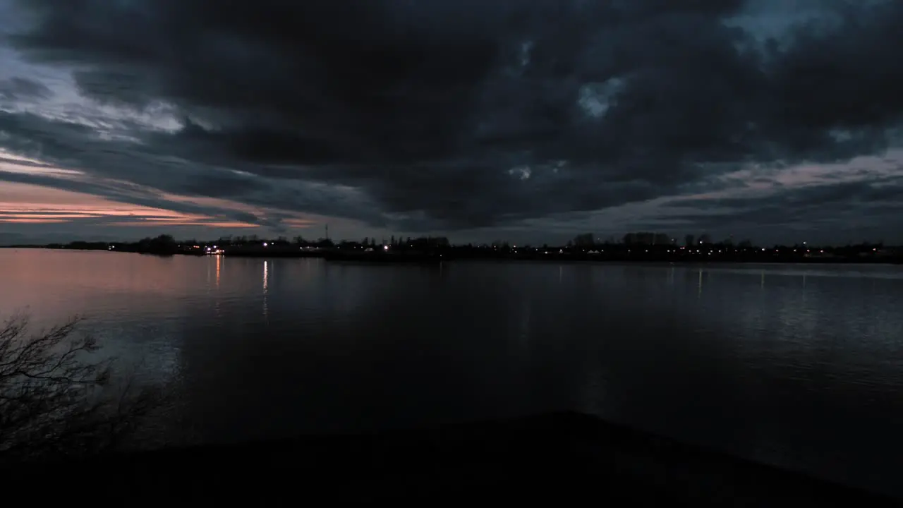 Pan right view of dark clouds over still river waters with dramatic clouds and colours in the sunset sky