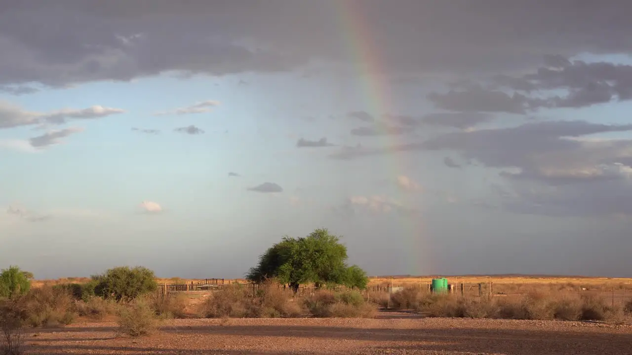 Still stable shot of a rainbow in the distance with a sheep enclosure in front on a sheep farm in Namibia