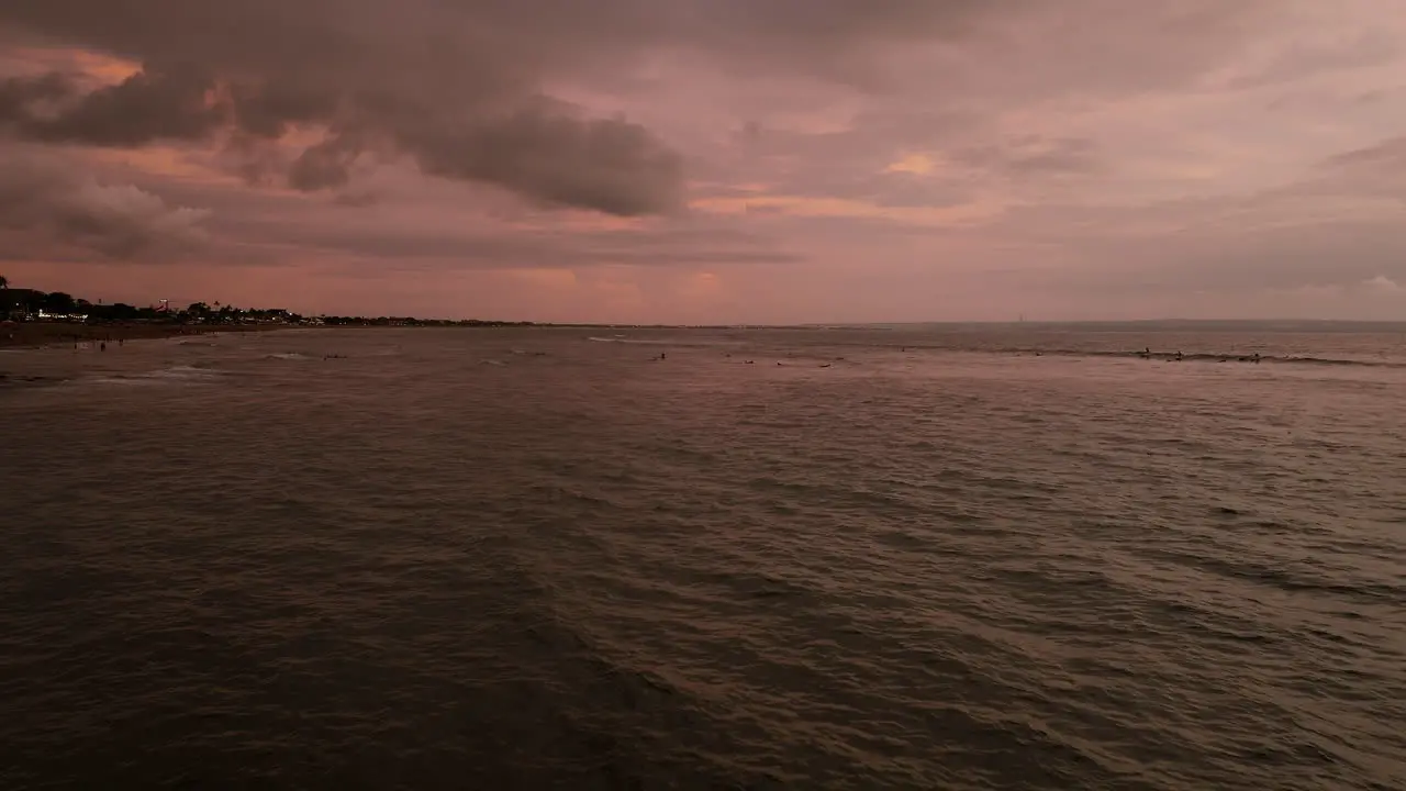 Ocean waves roll across bringing calm surfing waves under hazey red sky in Canggu Bali