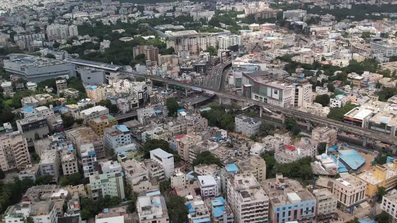 Aerial cinematic footage of a city in India shows buildings and trees paralleling railroad tracks and a metro station in the middle of the city