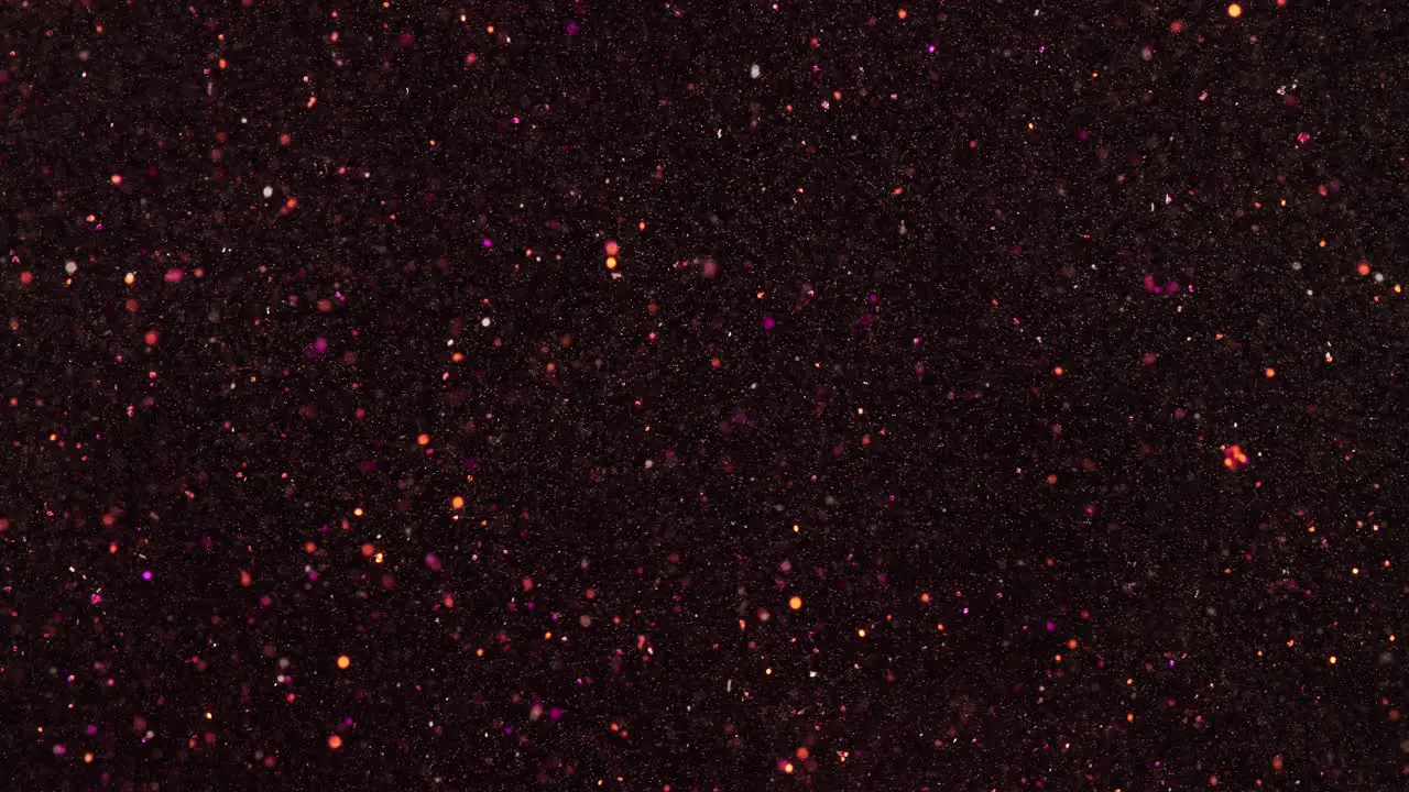 In slow motion pink and gold glitter particles move almost randomly against a black background