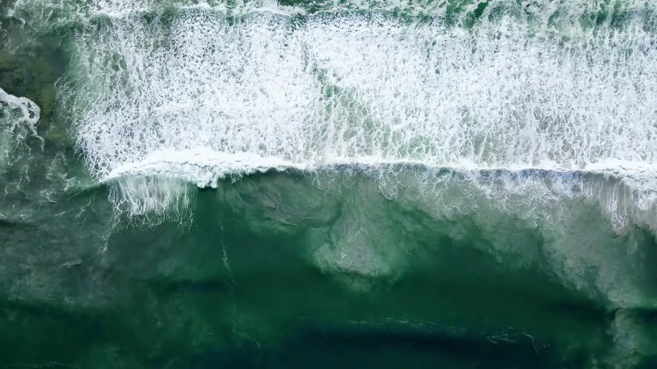 Aerial Waves rolling out white-wash with sandy bottom disturbed ascending drone shot