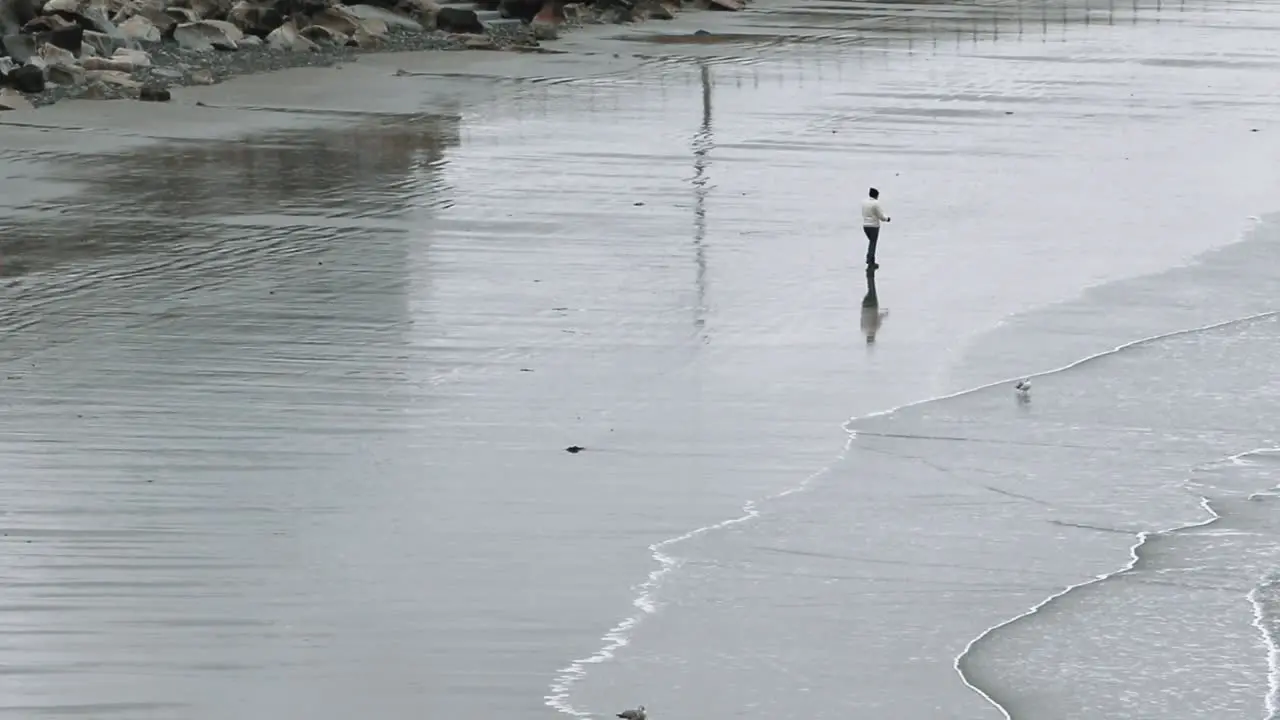 Lone person strolling up the beach on a cold day waves rolling ashore