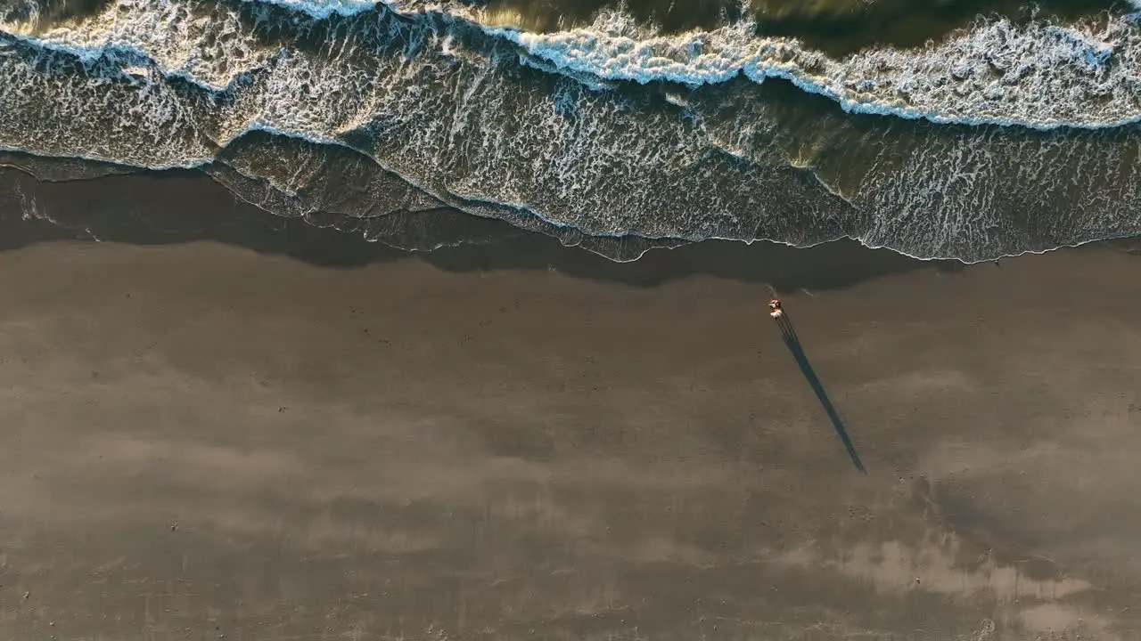 Aerial top down shot of couple walking alone sandy beach at sunset in Netherlands Waves of North Sea reaching shoreline