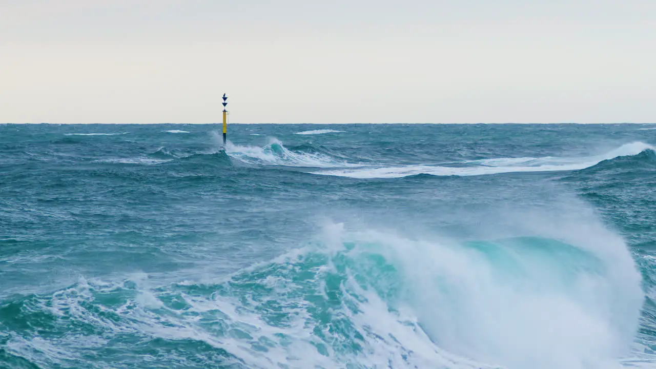 Big sea waves creating crest and crashing on cardinal mark with grebes sitting restless sea