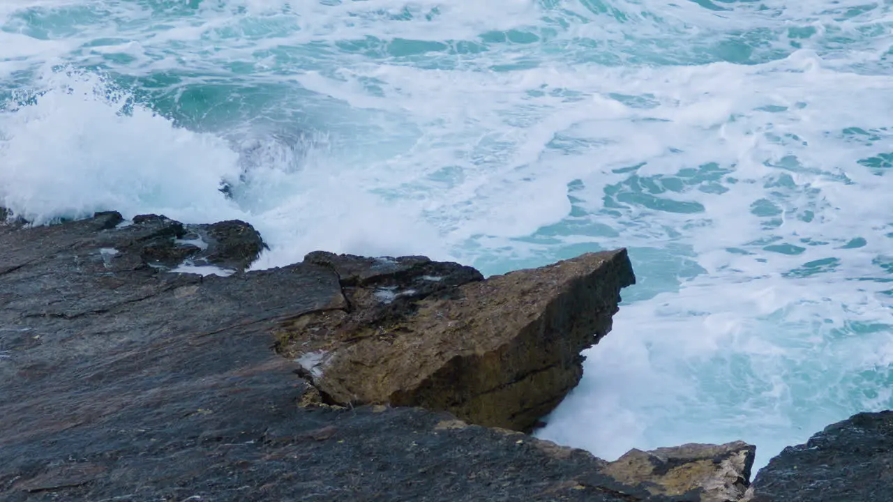 Sea waves breaking on rocky shore creating foam and mist on stormy weather close up