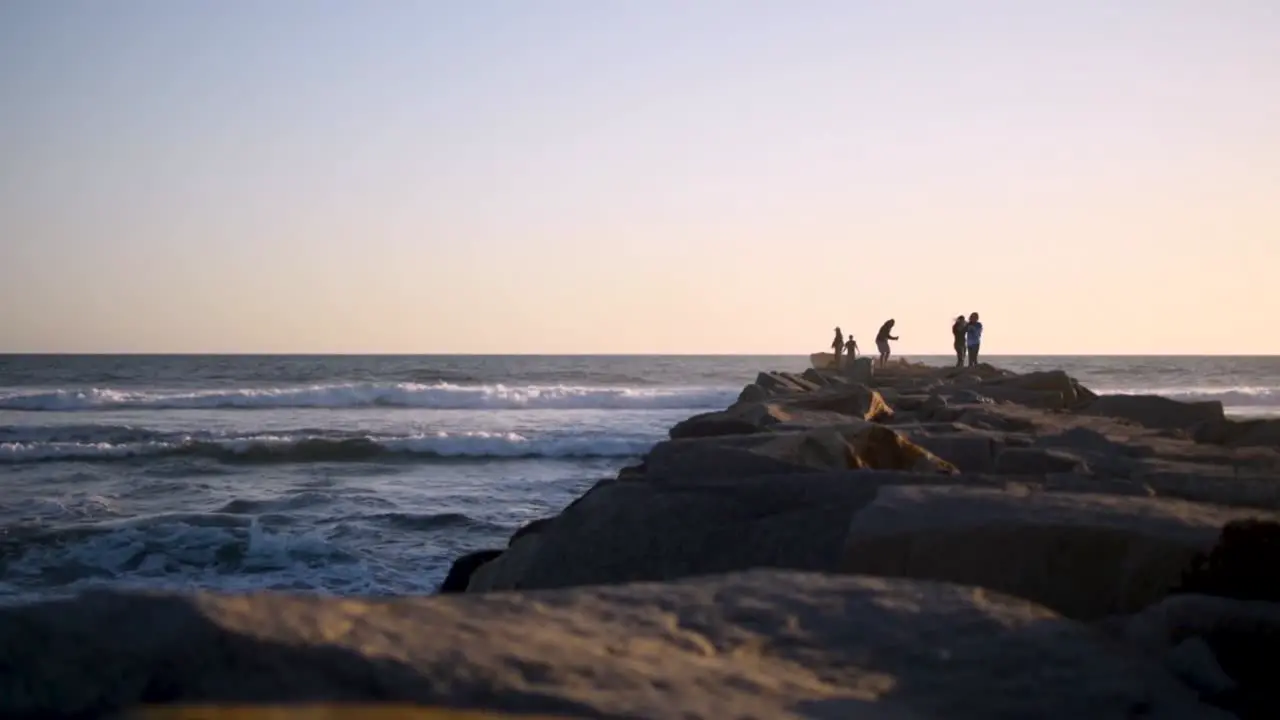 Beautiful calm and peaceful sunset in San Diego shooting down a jetty with people and waves crashing alongside it