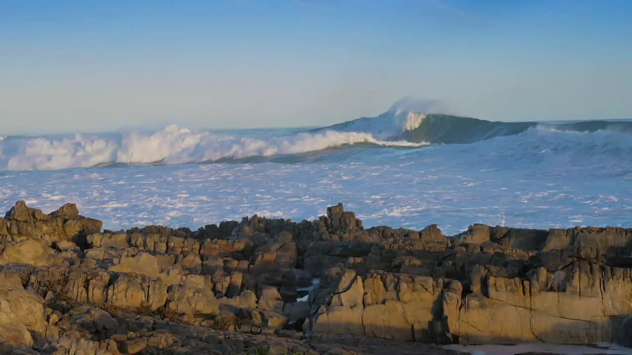 Huge waves rolling in onto rocky coastline blue skies