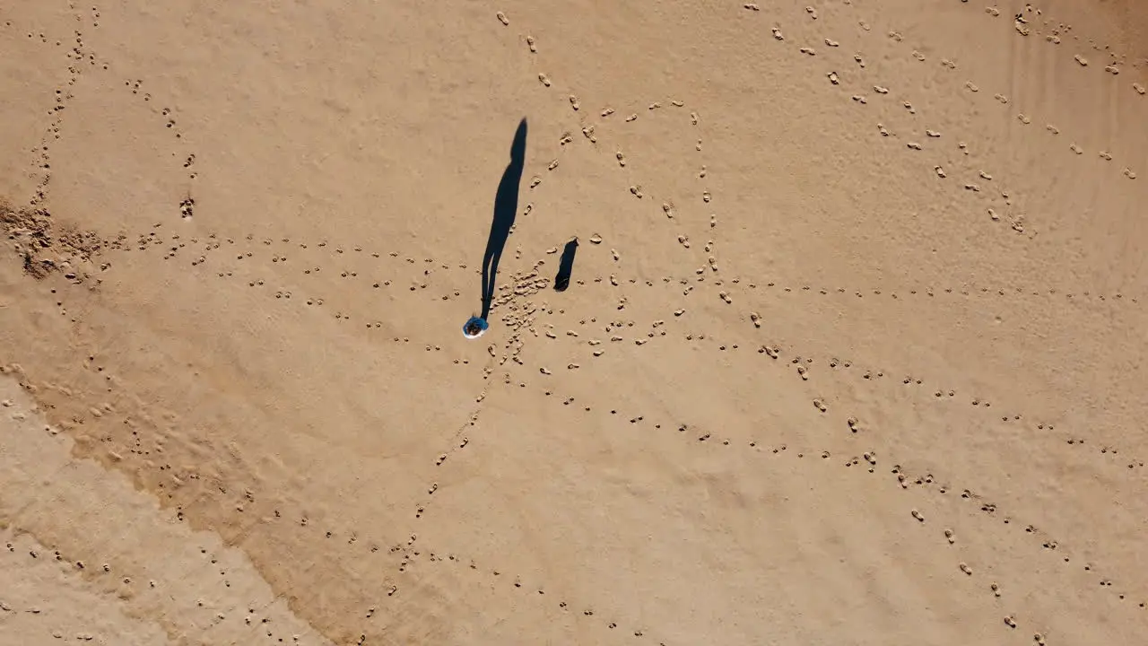 Aerial footage captures person leisurely walking on a sun-drenched sandy beach