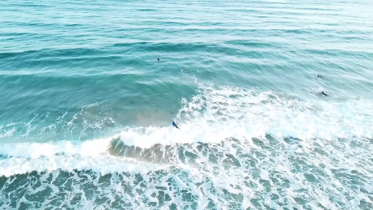 Drone aerial of surfer catching a wave in blue water on a sunny summer day