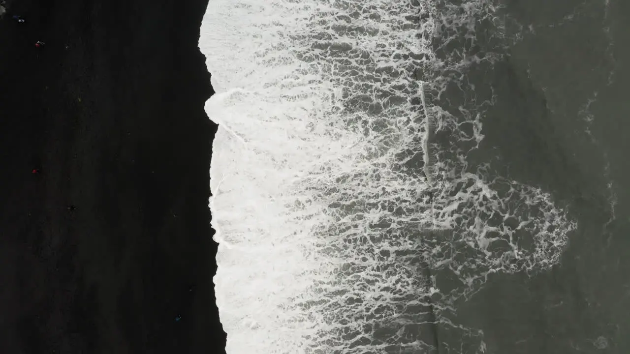 Top down aerial view of foamy waves splashing on Reynisfjara black sand beach in Iceland