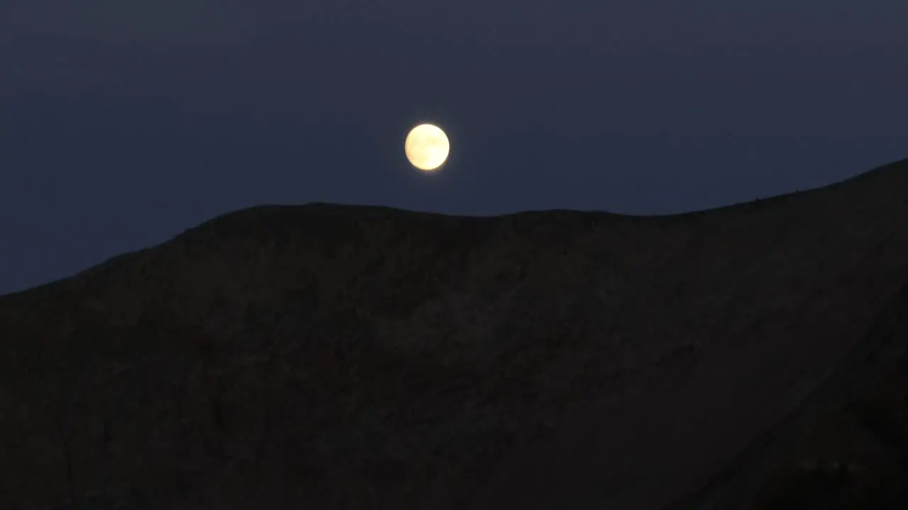 A full moon falls behind a ridge line in the Colorado Rockies at night