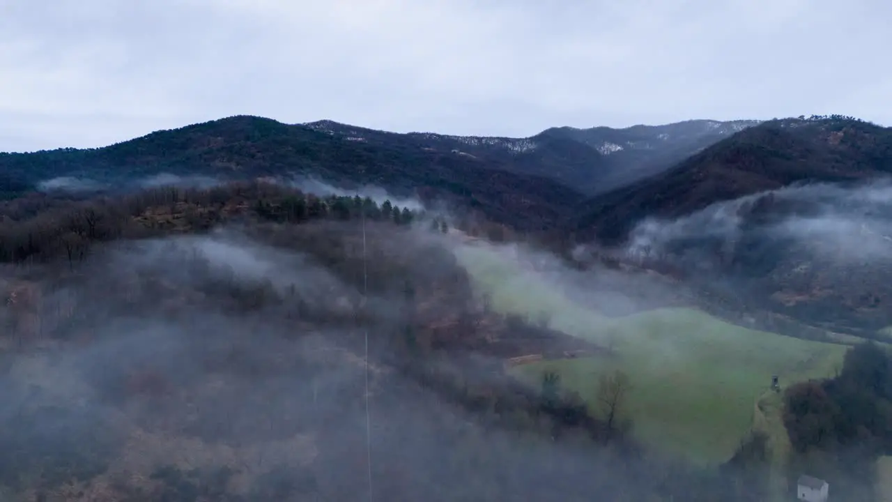 Mist clouds over hilly countryside landscape below gray sky timelapse