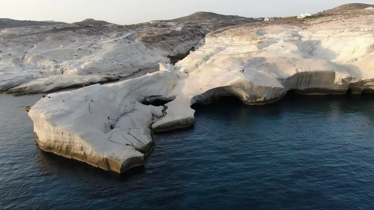 Drone view in Greece flying over a moon shaped white rock area in Milos island at sunrise next to the dark blue sea