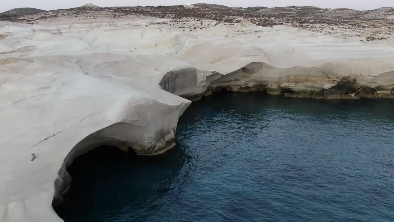 Drone view in Greece flying over a moon shaped white rock area straight arc in Milos island at sunrise next to the dark blue sea