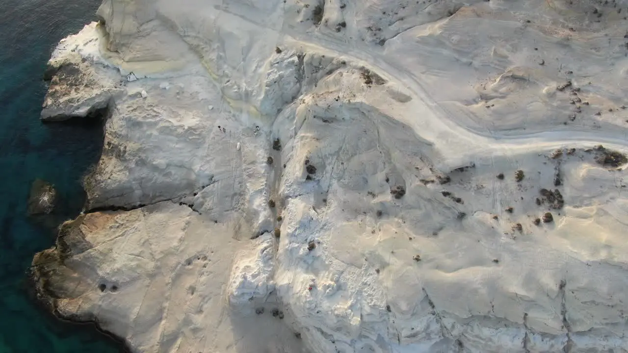 Drone view in Greece flying over a moon shaped white rock and clear blue water top view in Milos island at sunrise next to the dark blue sea